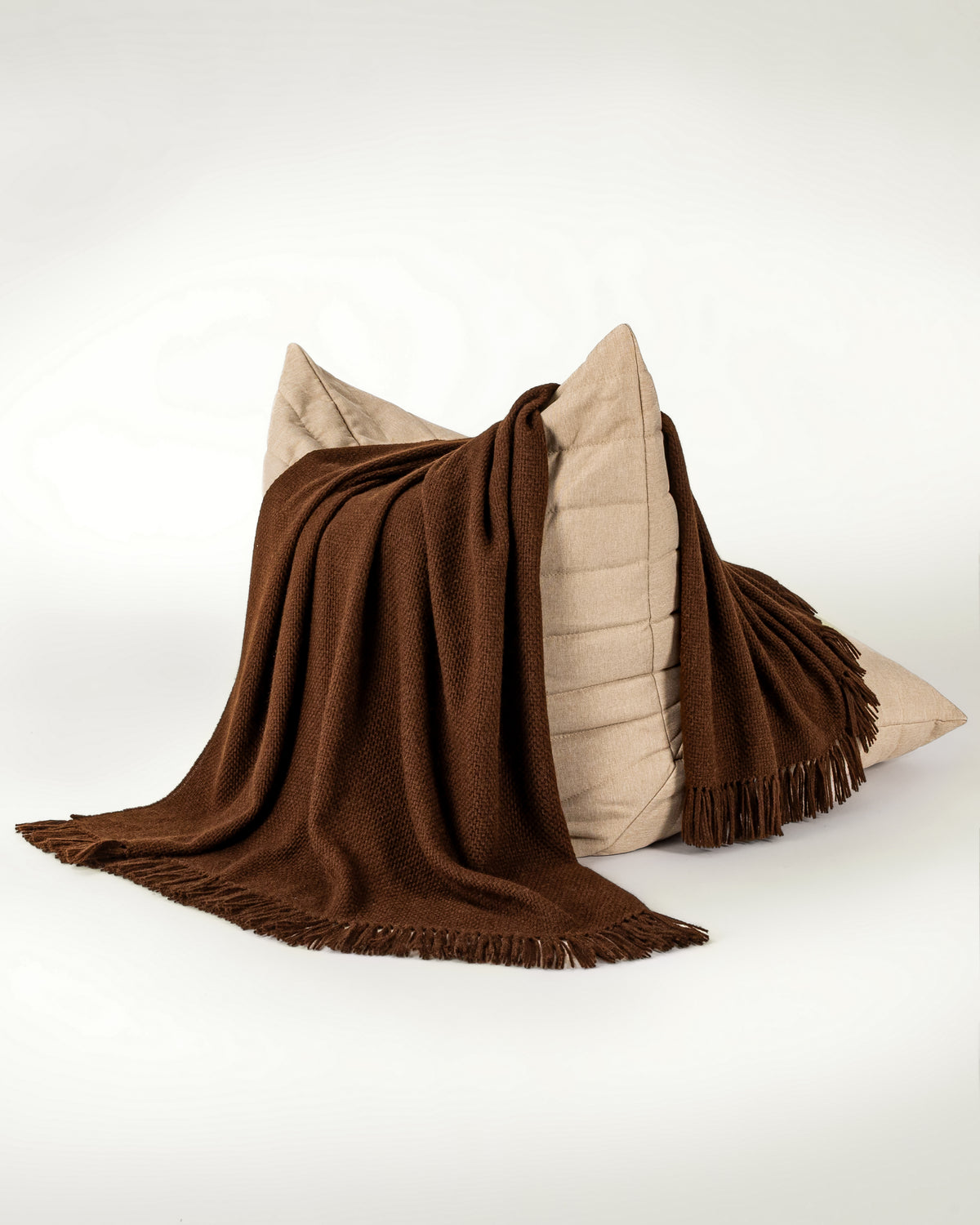 Normy Alpaca Blanket in cocoa draped over a beige chair on a clean white studio background.
