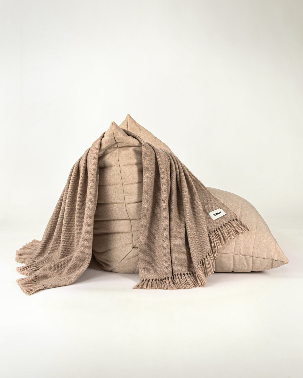 Normy Alpaca Blanket in clay draped over a beige chair, set against a clean off-white studio background.