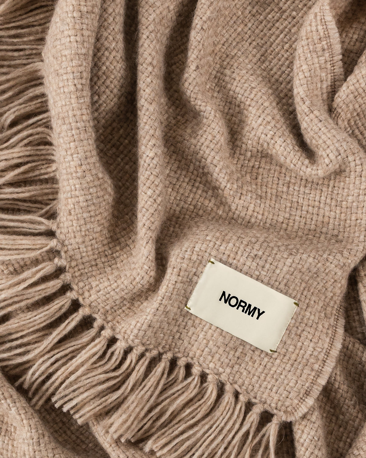 A close-up of Normy Alpaca Blanket in clay with a small cream fabric label reading NORMY.