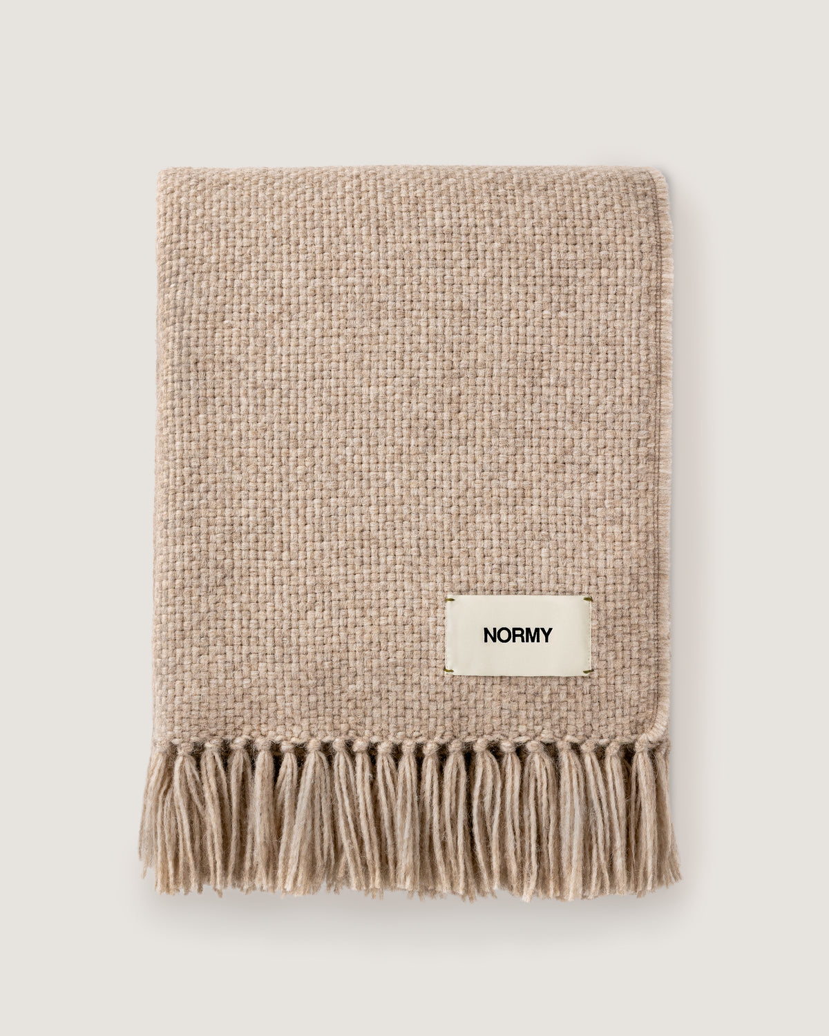 Normy Alpaca Blanket in clay with a small cream label reading NORMY, photographed flat against a light warm gray background.