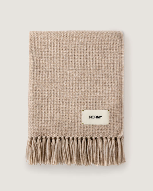 Normy Alpaca Blanket in clay with a small cream label reading NORMY, photographed flat against a light warm gray background.