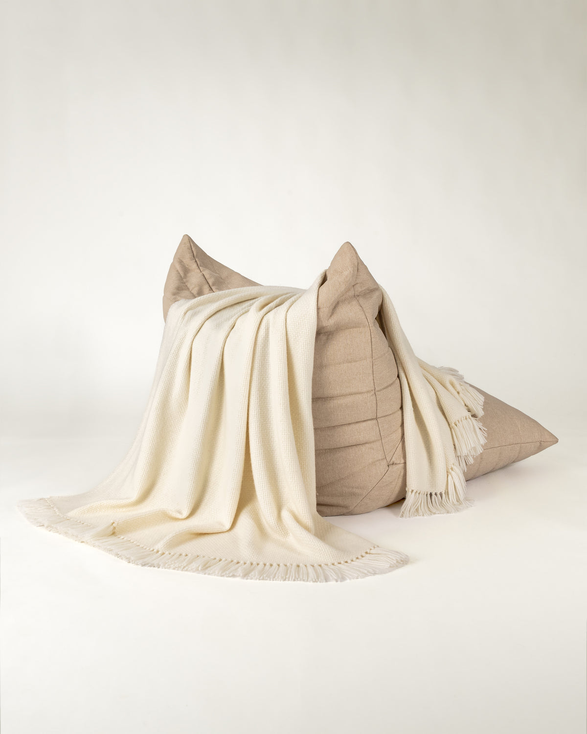 Normy Alpaca Blanket in moon draped over a beige chair set against a seamless light gray studio background.