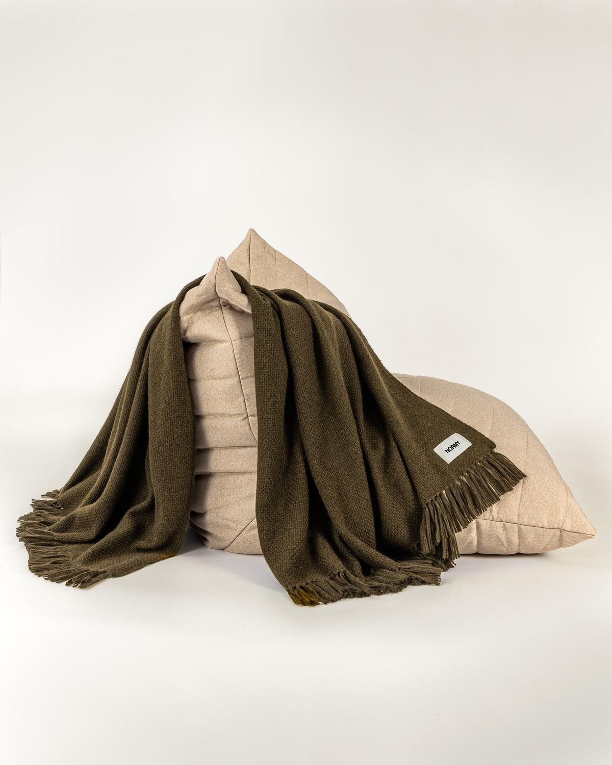 Normy Alpaca Blanket in olive draped over a beige chair on a white studio background.