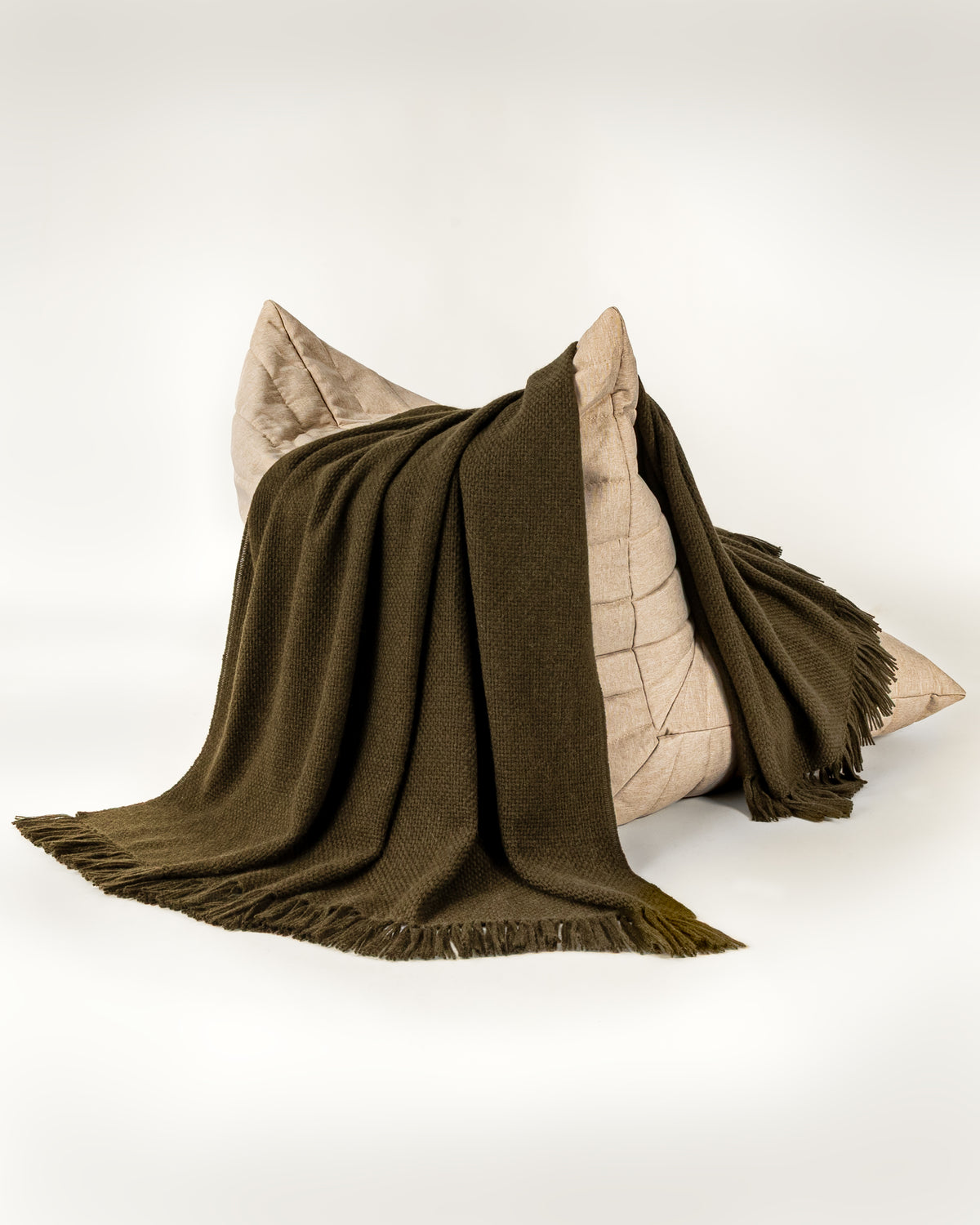 Normy Alpaca Blanket in olive draped over a light beige chair, set against a clean white studio background.